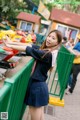 A woman in a school uniform standing next to a green fence.