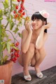 A woman kneeling down next to a potted plant with tomatoes.