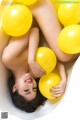 A woman laying in a bathtub filled with yellow balloons.