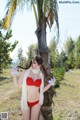 A woman in a red bikini standing next to a palm tree.