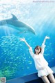 A woman standing in front of a large aquarium with a dolphin.